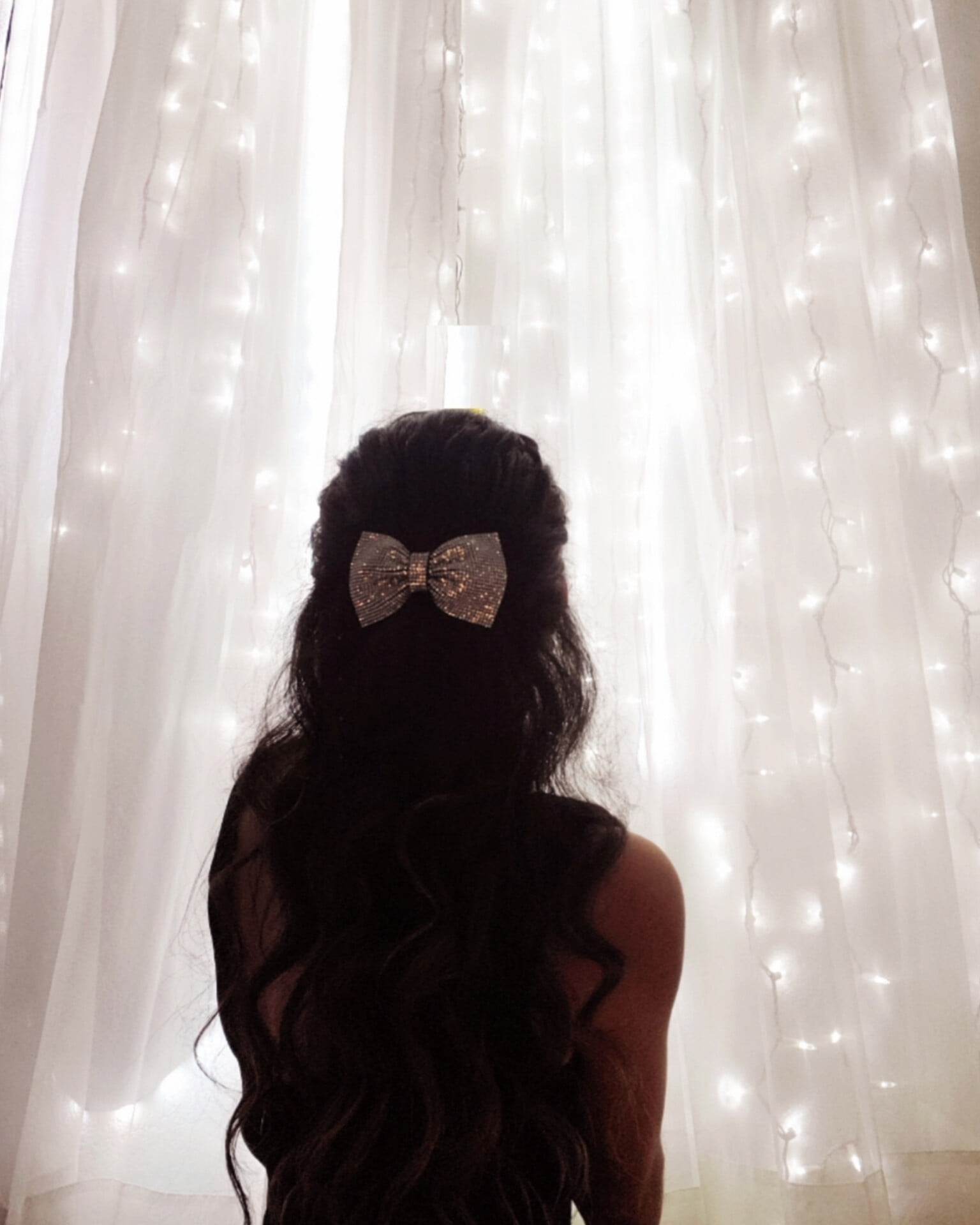 girl facing a wall filled with white lights behind a white curtain